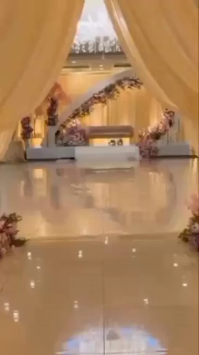 Blush curtains opening onto a reflective floor and a stage framed by a floral arch