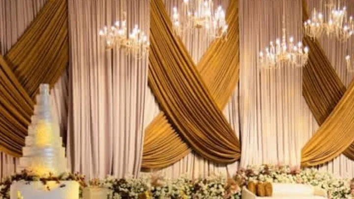 Crossed gold and blush drapery with crystal chandeliers above a flower-lined stage